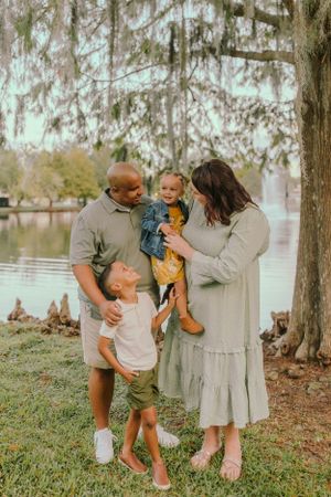 Candid family portrait with everyone laughing together outdoors by a lake.