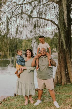 Joyful family photo session with everyone embracing and laughing by the water.