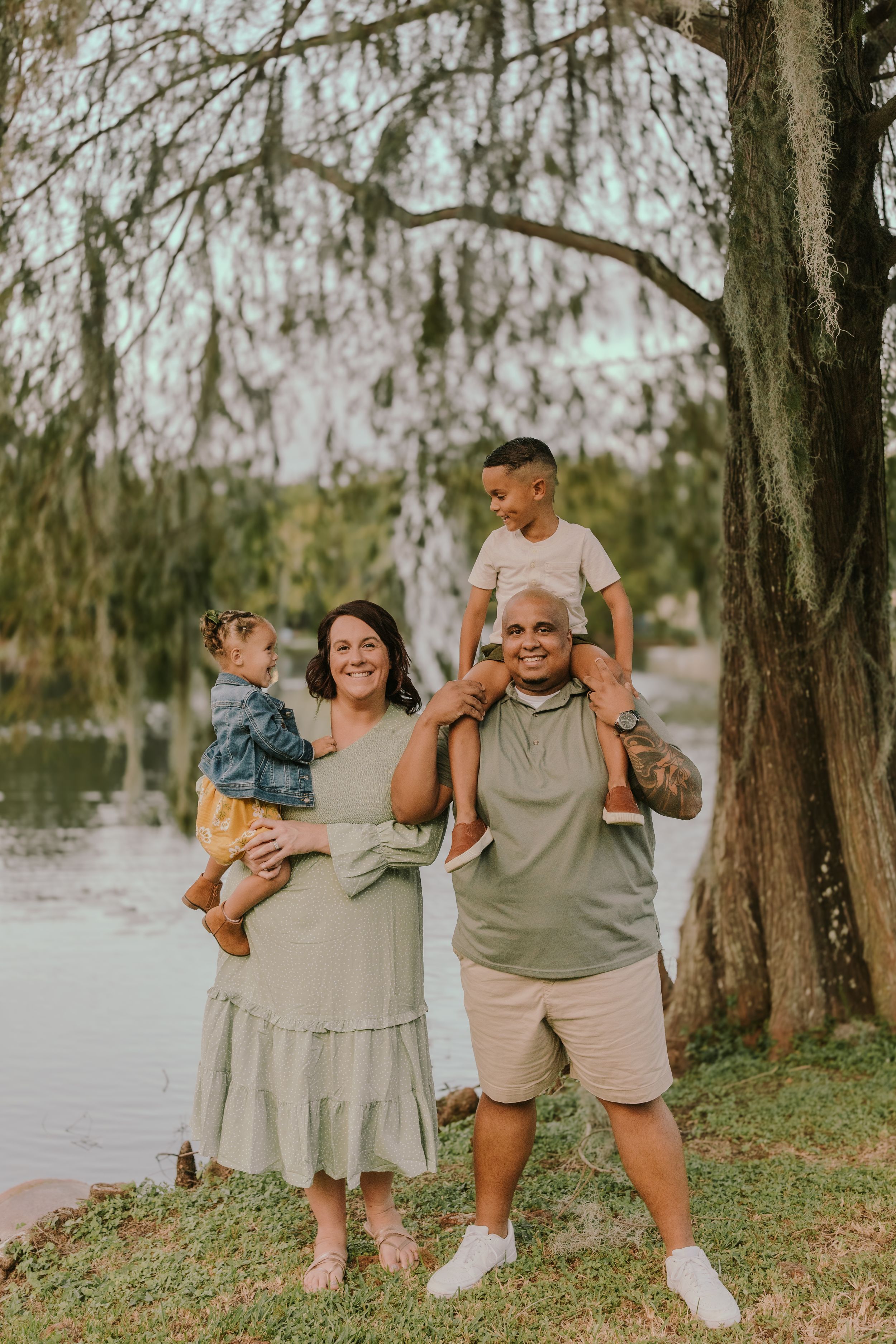 Joyful family photo session with everyone embracing and laughing by the water.