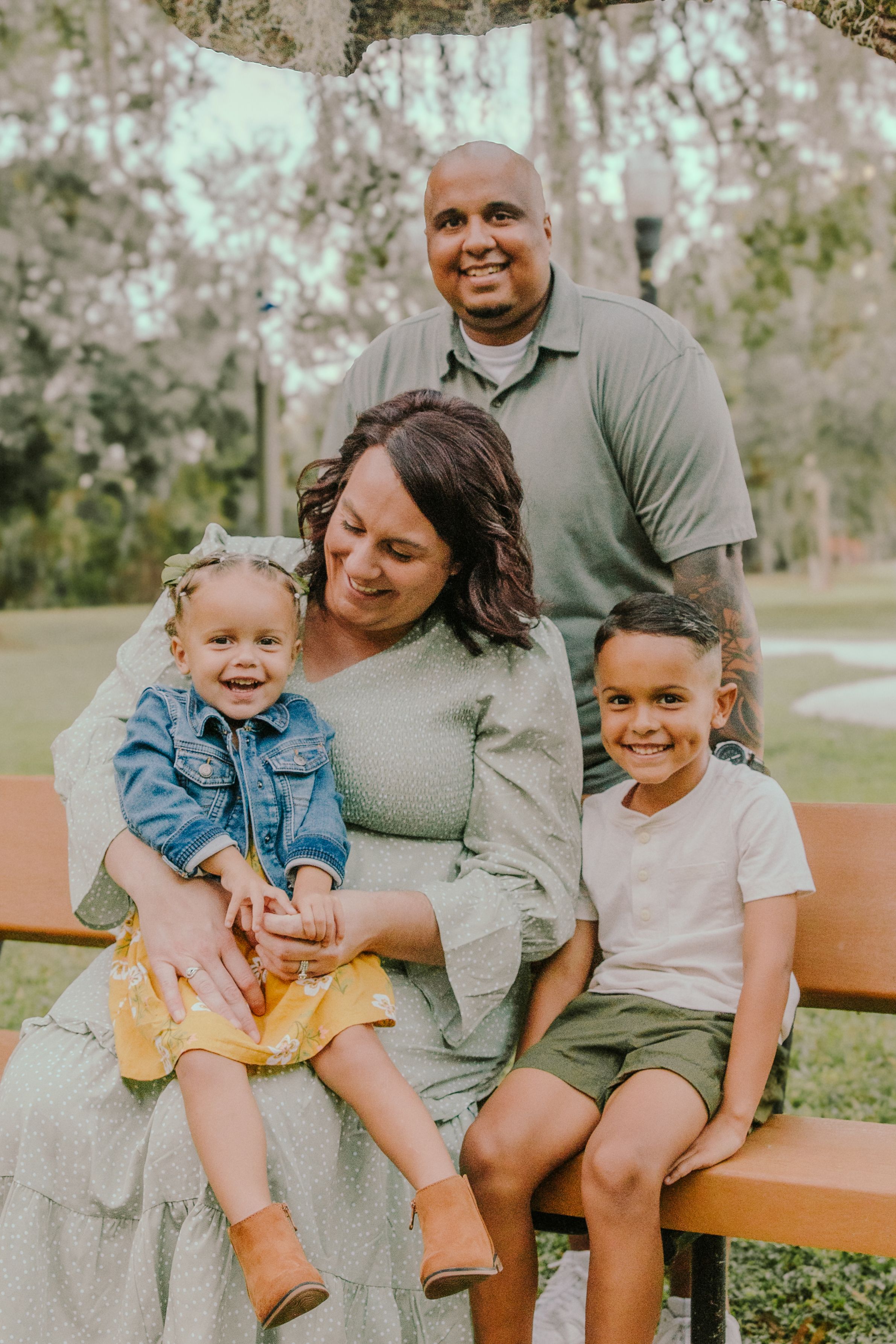Family enjoying a playful moment together on a wooden bench in a park setting.