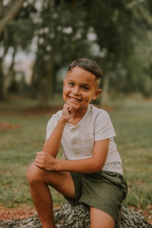 A child sits casually on a tree branch while smiling at the camera.
