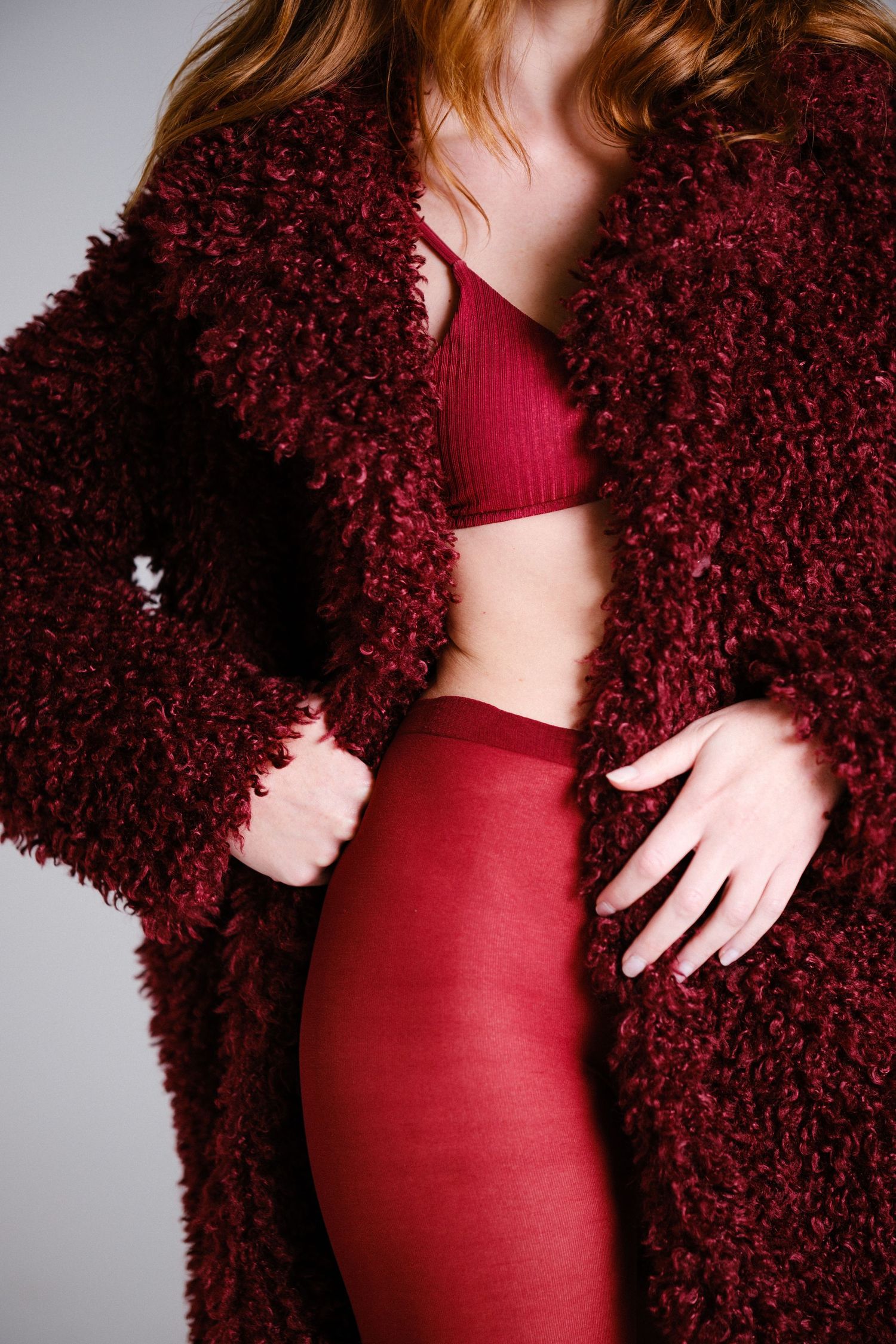 Close-up fashion shot of burgundy textured coat and fitted bodysuit ensemble.