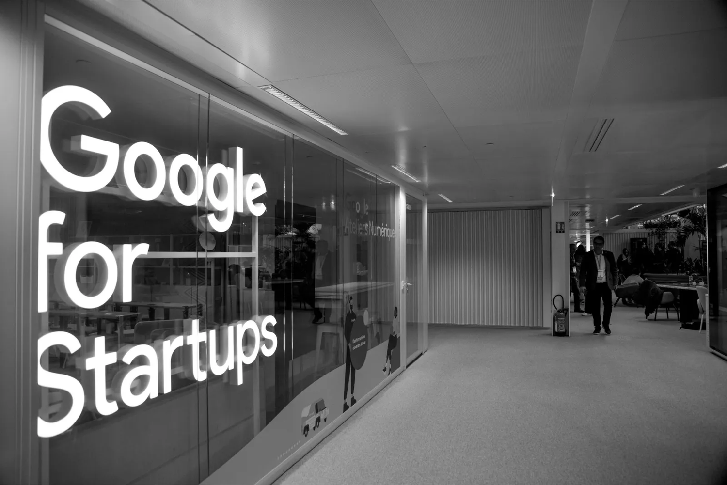 Photographie en noir et blanc d’un espace d’accueil moderne avec un grand néon “Google for Startups” au mur.
