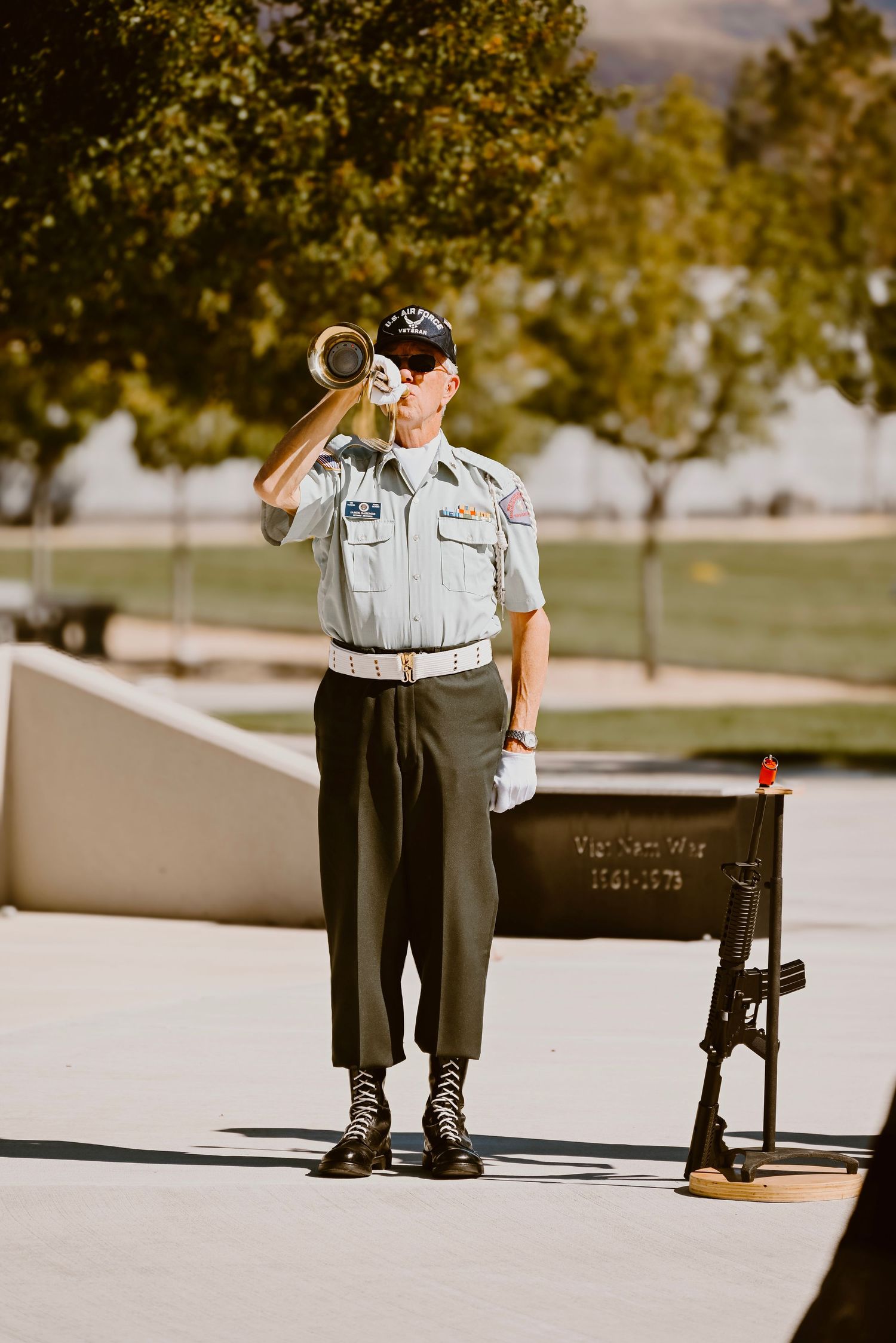 Military member playing bugle during ceremonial duty outdoors.