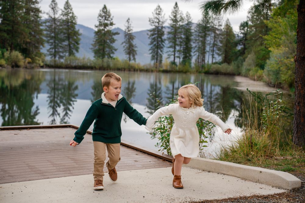 brother and sister run together by the pond action portrait