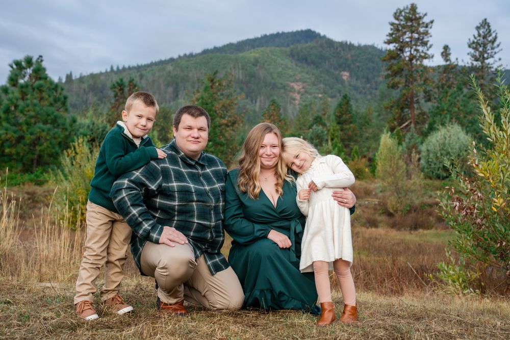 family of 4 Christmas portrait with the mountains behind them and evergreen trees