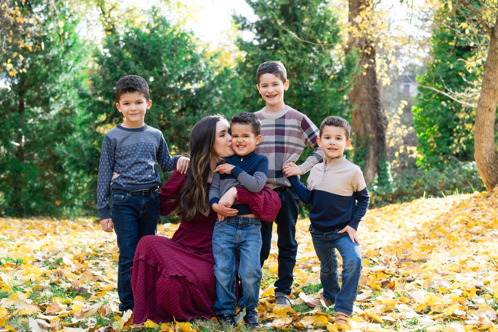 Mom kisses youngest in a portrait with mom and her four boys with fall leaves behind them