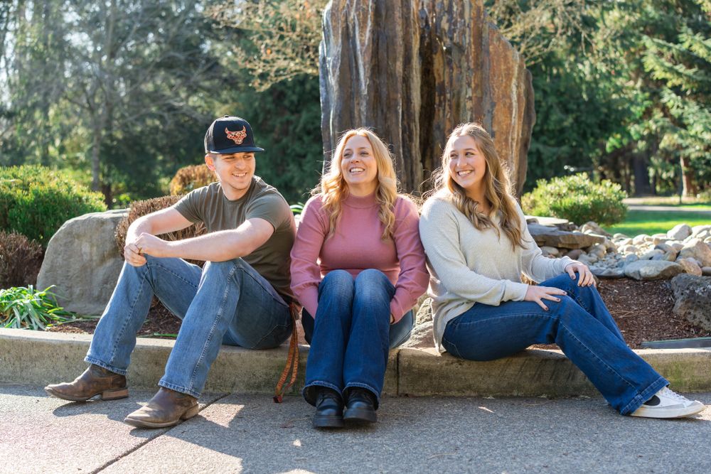 Family Portrait with mom and older kids sitting and laughing together by the fountain feature at the park.