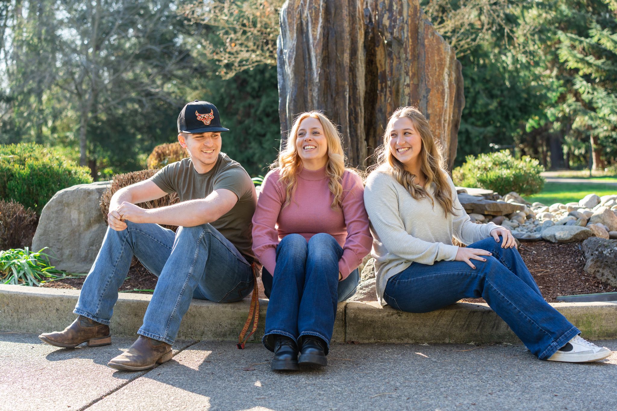 Family Portrait with mom and older kids sitting and laughing together by the fountain feature at the park.
