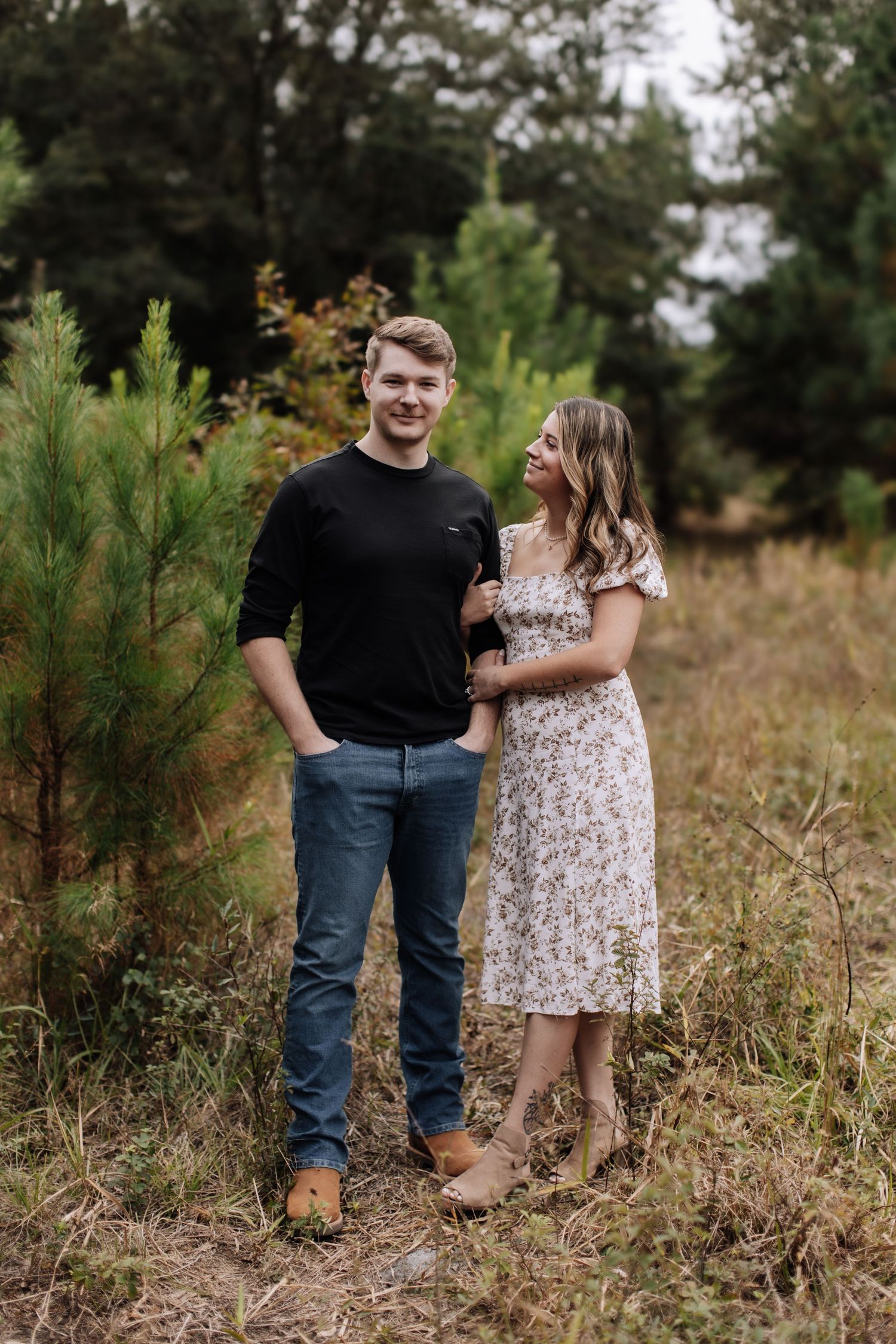 A couple shares a romantic moment sitting in a sun-drenched field at golden hour while dressed in casual summer attire.