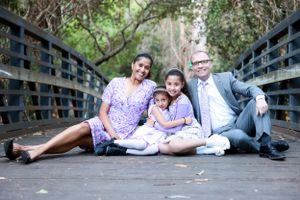 Joyful family of four sitting on wooden bridge, parents with two girls in matching purple outfits.