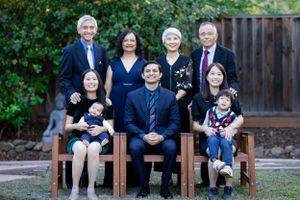 Multigenerational Asian family portrait with eight members seated and standing outdoors on a sunny day.