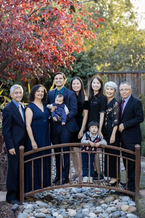 Extended multigenerational family of eight posing on a decorative garden bridge surrounded by colorful foliage.