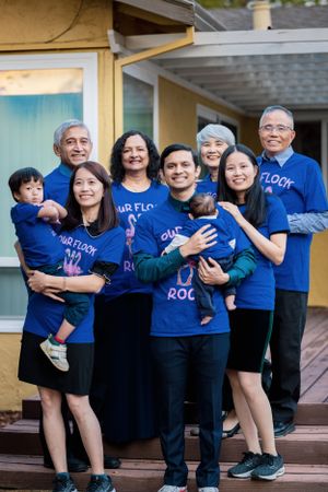 Multigenerational family wearing matching blue Our Flock Rocks t-shirts, posing together on a home porch.