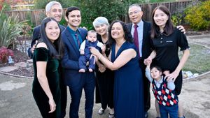 Large multigenerational Asian family gathered outdoors, smiling together with two young children and a baby.