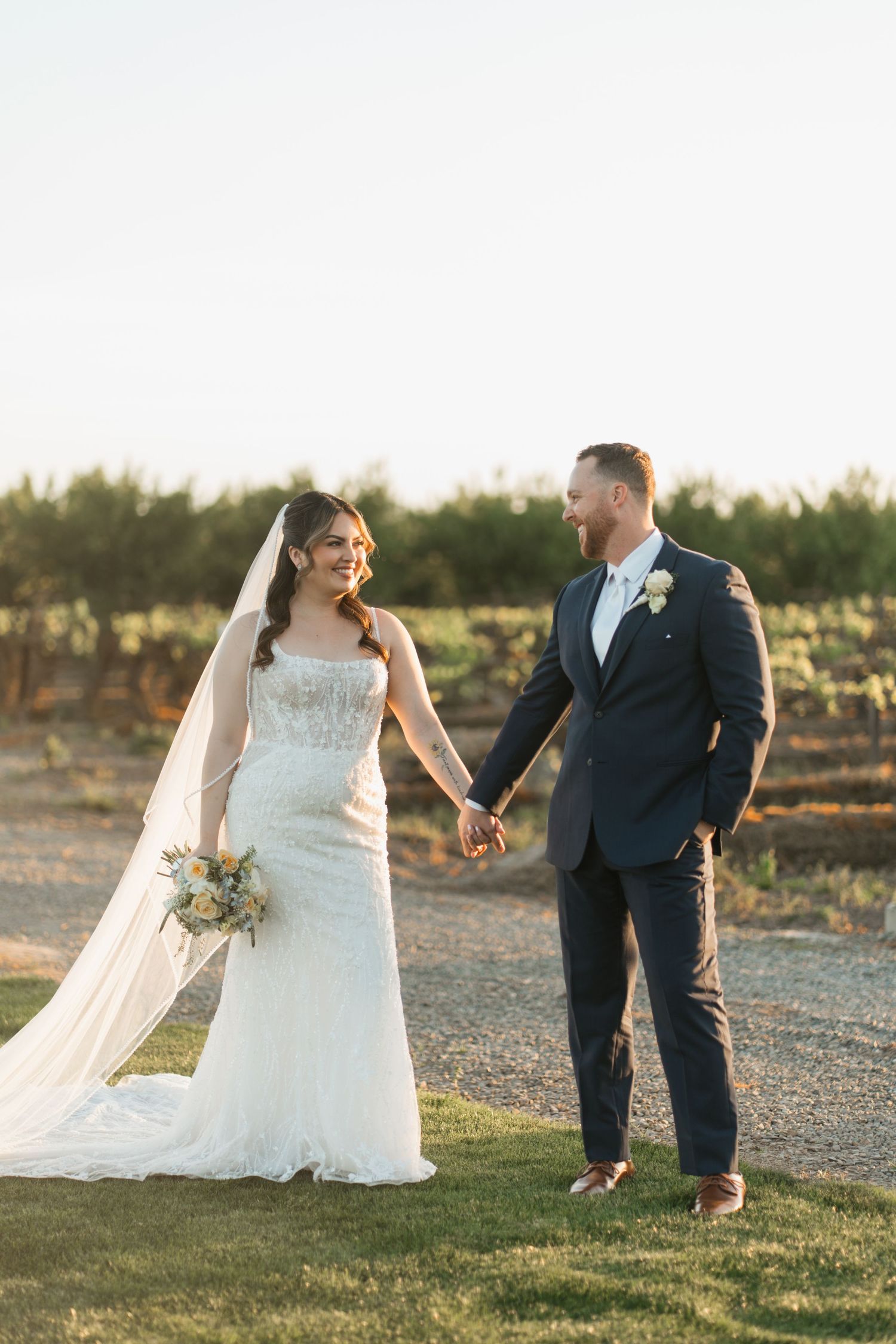 A couple shares a romantic moment on a lawn with a beautiful tree backdrop at sunset.
