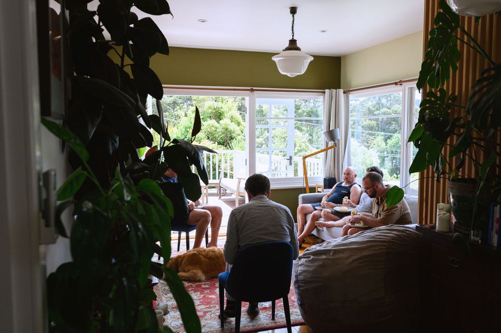 People gathered around a dining table in a sunny room with houseplants.