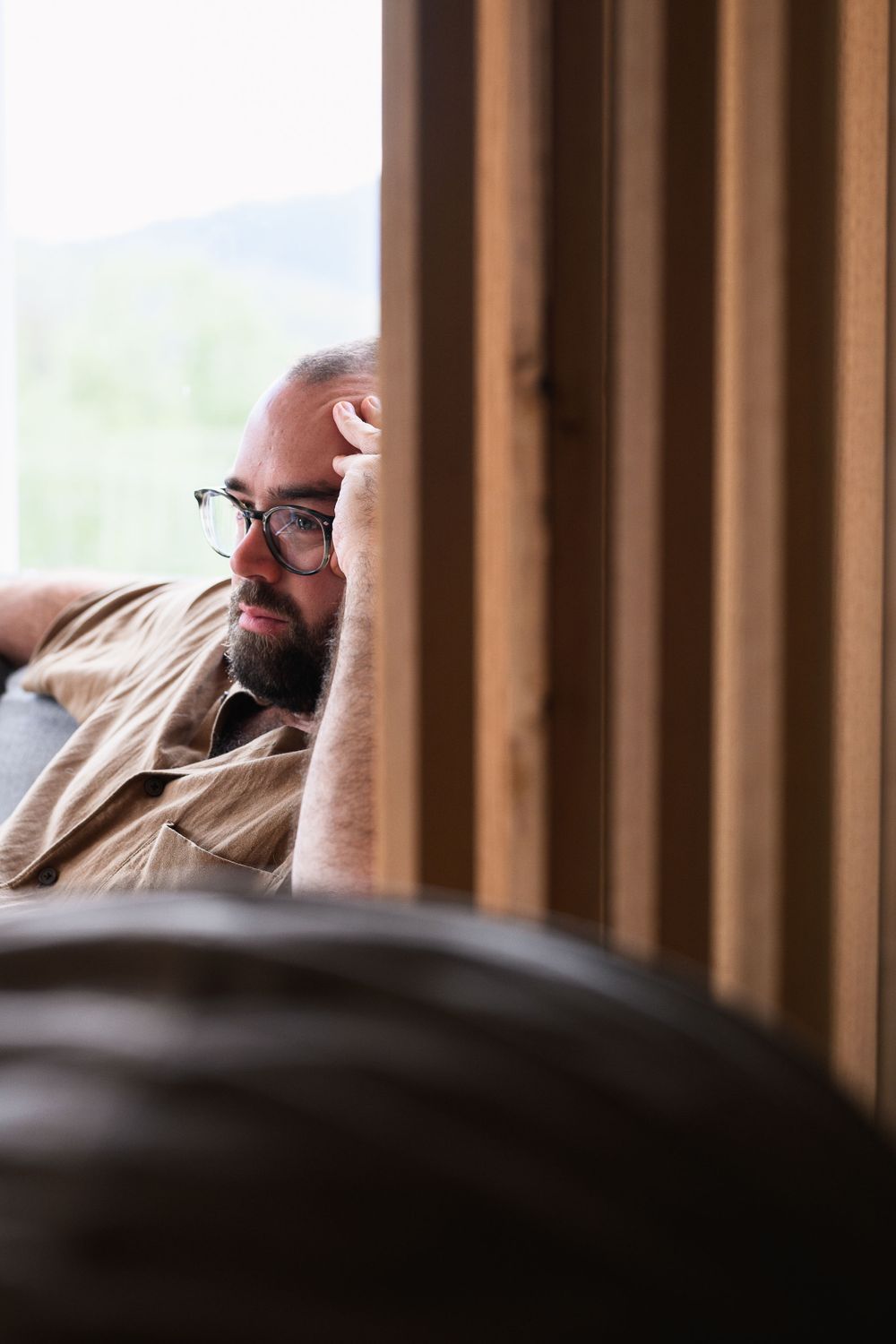 Candid portrait through wooden slats of someone resting in casual attire.