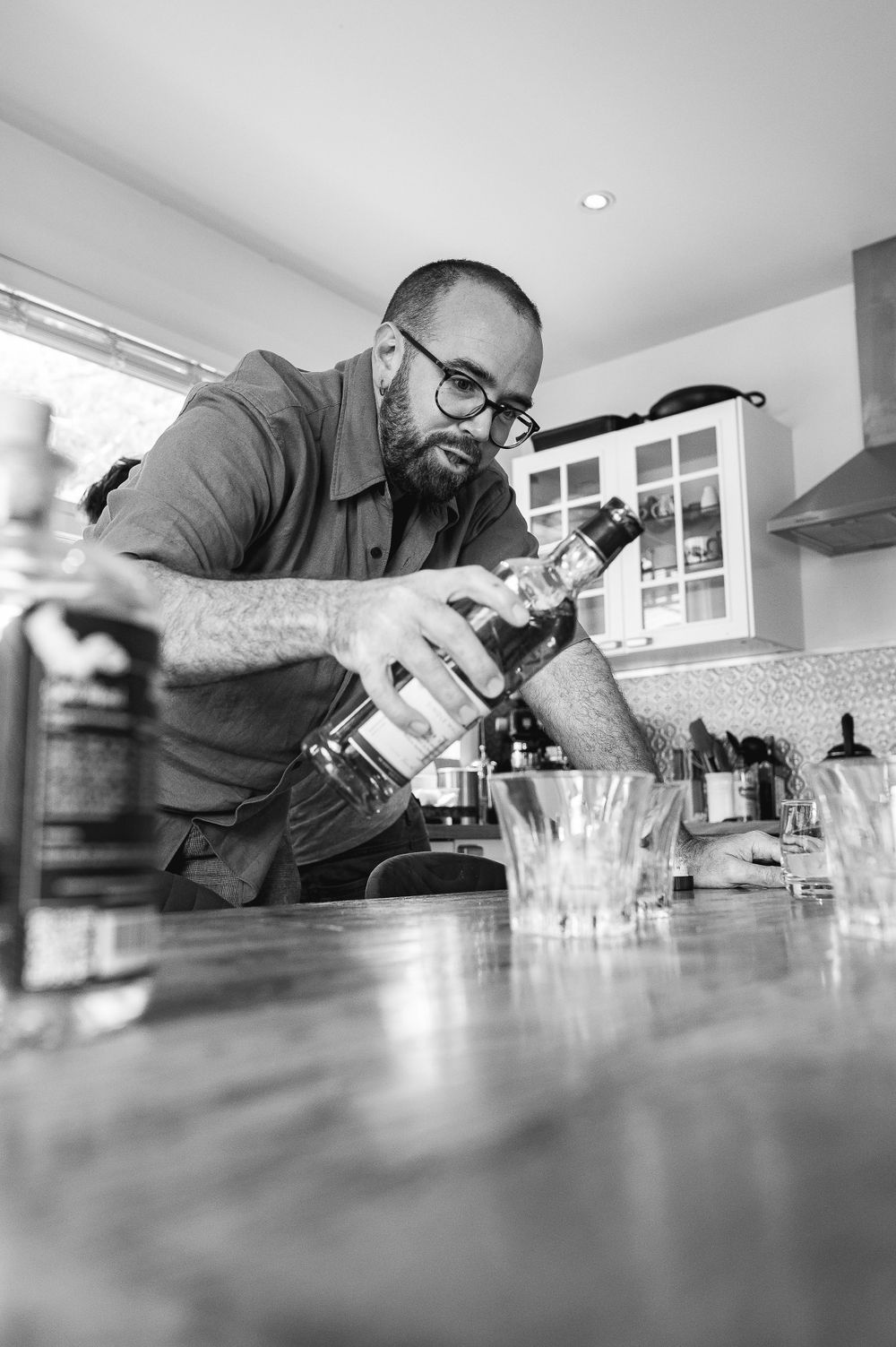 A bartender carefully pours a drink at a modern kitchen counter in black and white.