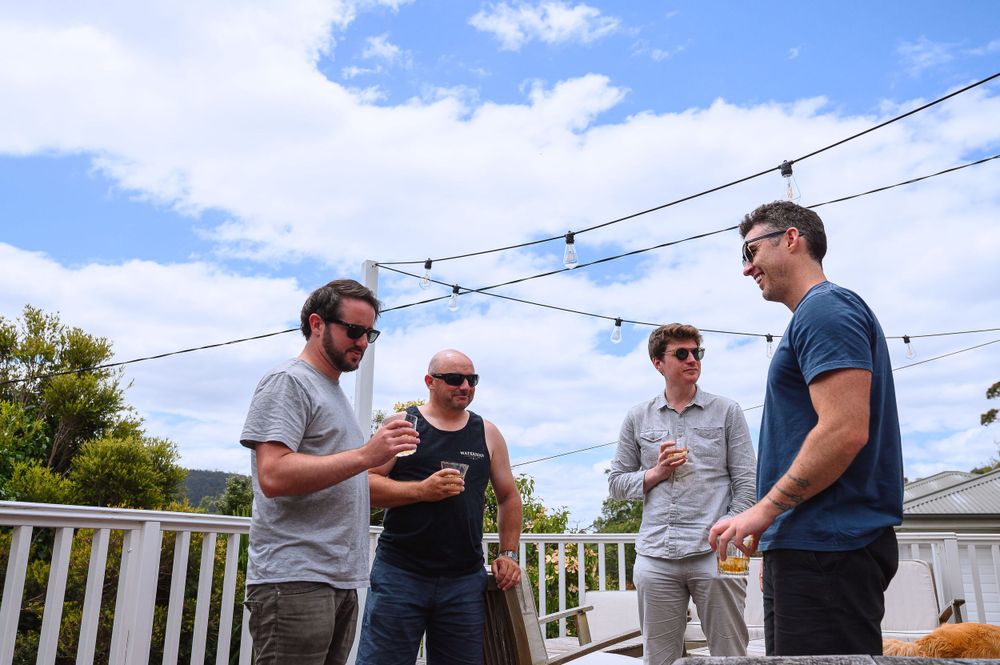 A group gathers on an outdoor deck with string lights overhead on a sunny day.