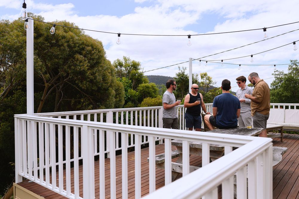 People gathered on a white-railed deck with string lights and greenery in the background.