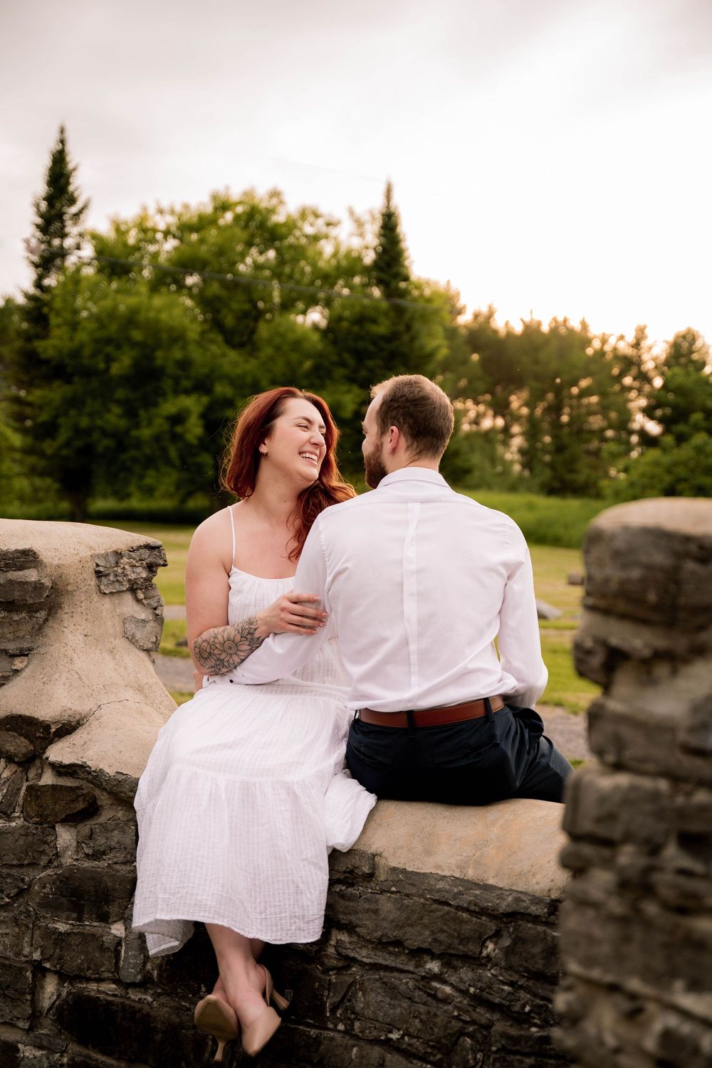 Romantic couple sits together on rocky ledge during golden hour sunset at scenic overlook.