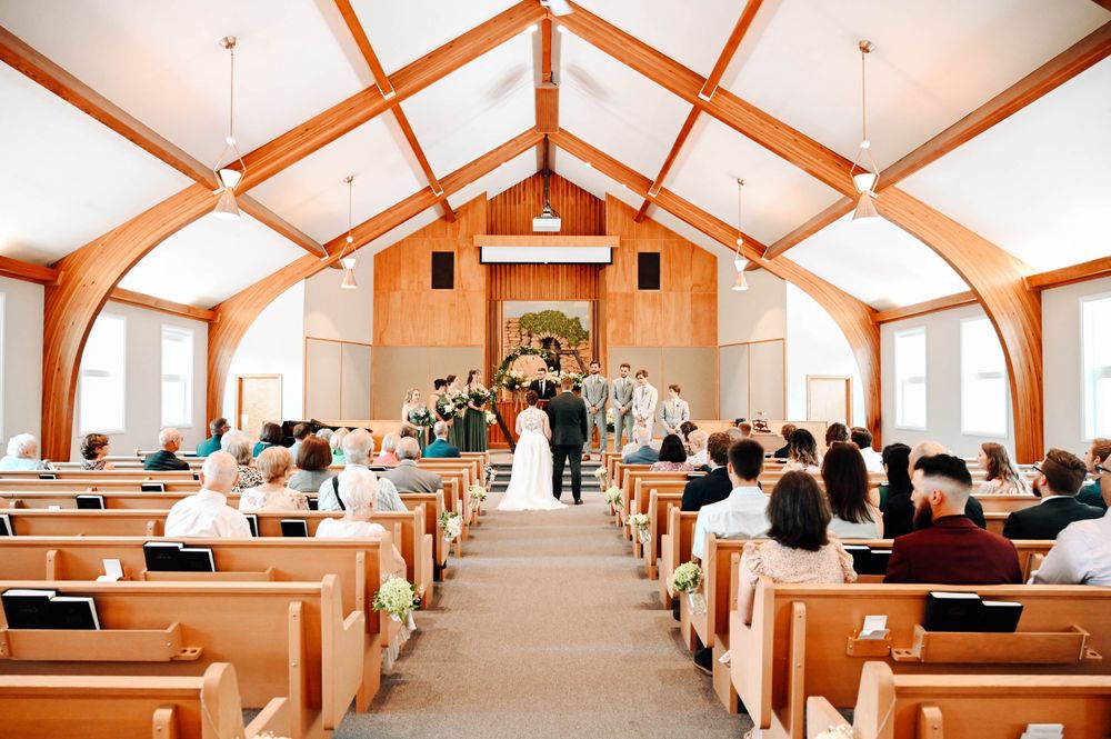 Traditional church wedding ceremony with wooden pews and vaulted ceiling filled with guests.
