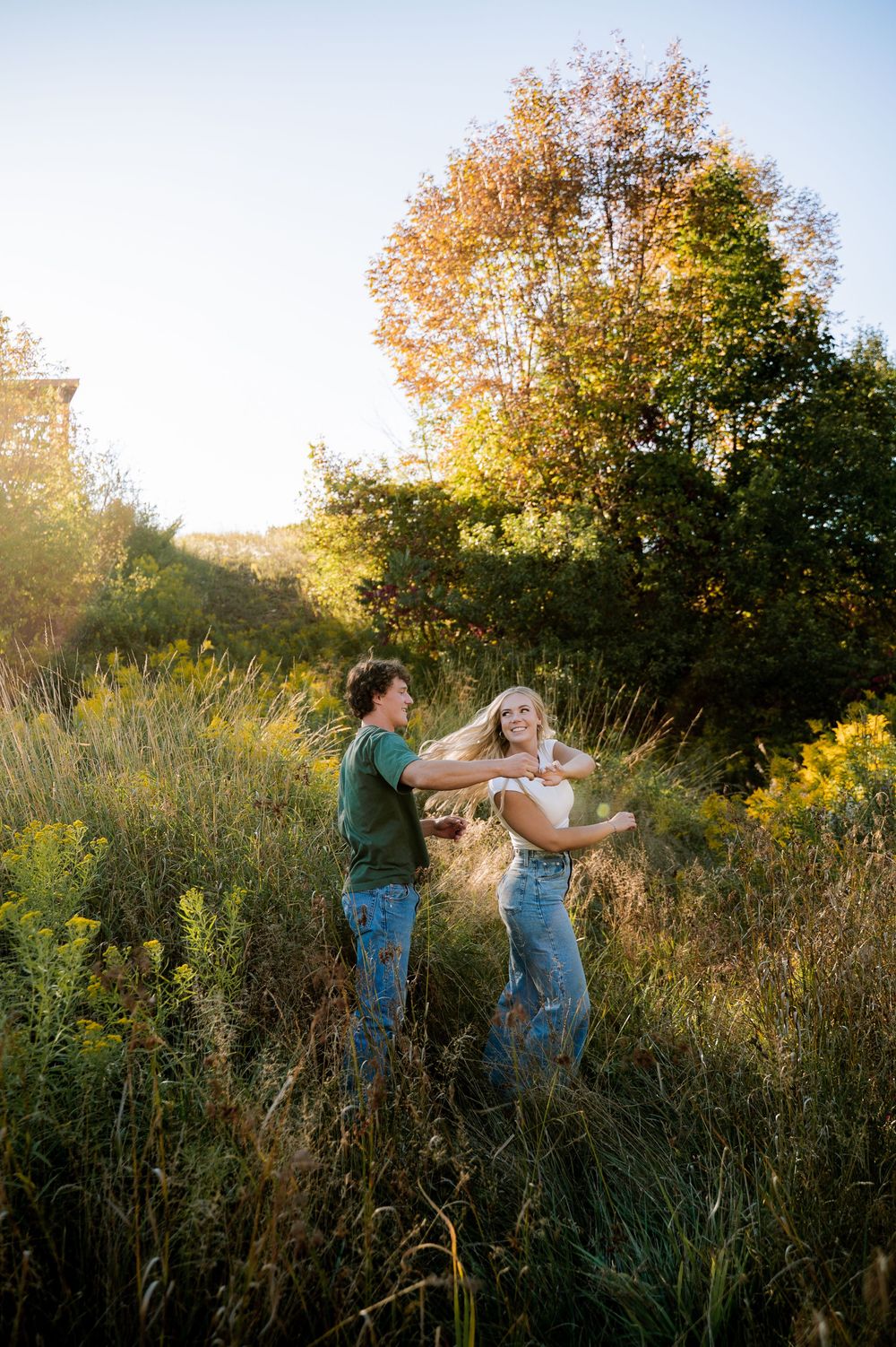 Two people dance and twirl together in a golden autumn meadow at sunset with trees in the background.