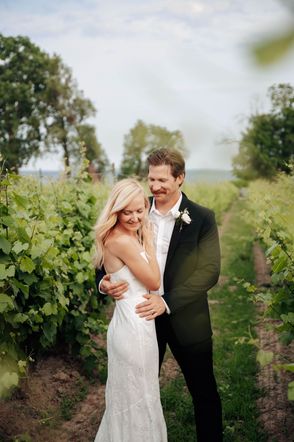 A couple shares intimate moments together while walking through lush green vineyard rows on a bright summer day.