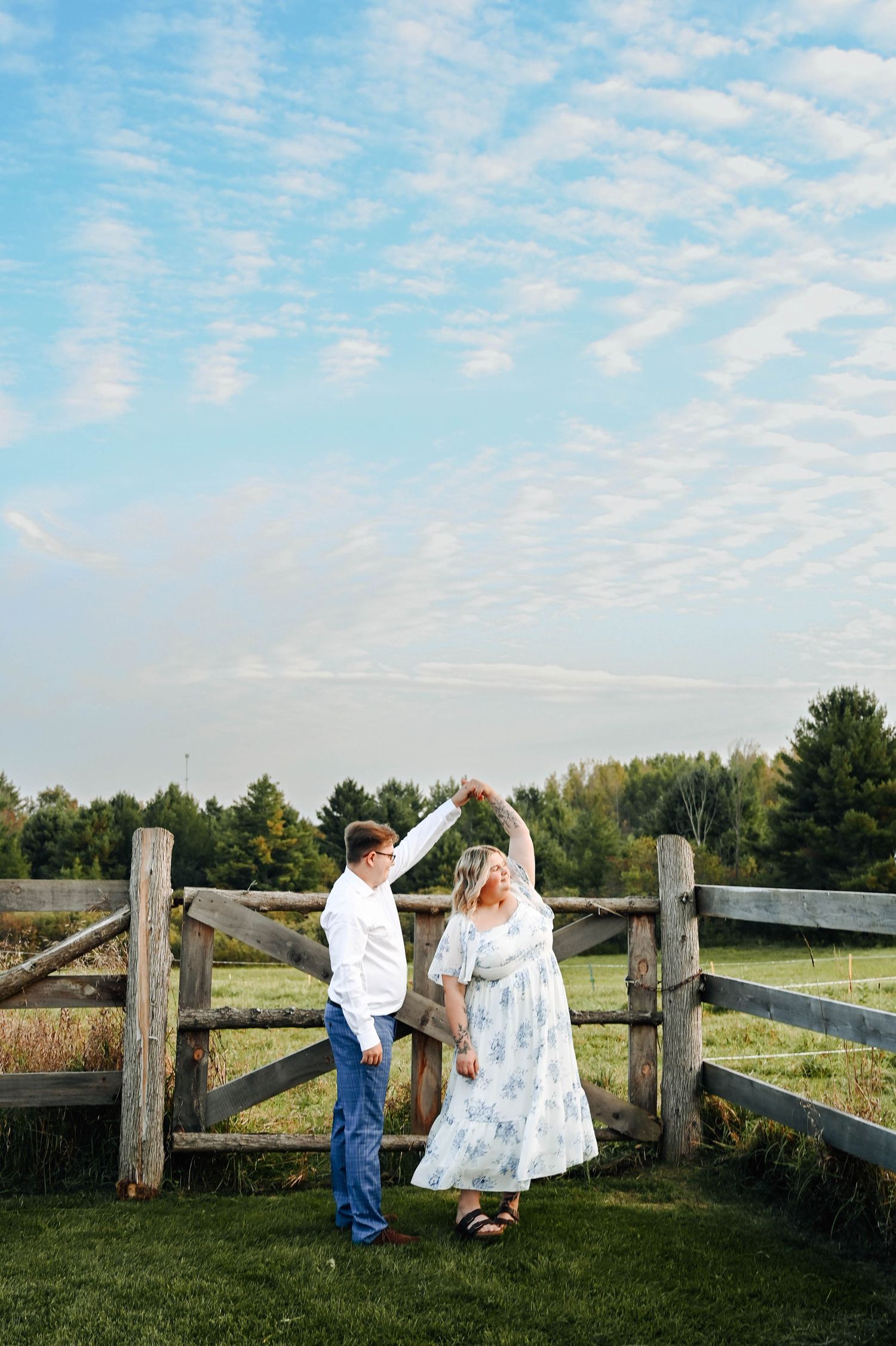 Couple dancing by rustic wooden fence under beautiful cloudy sky.