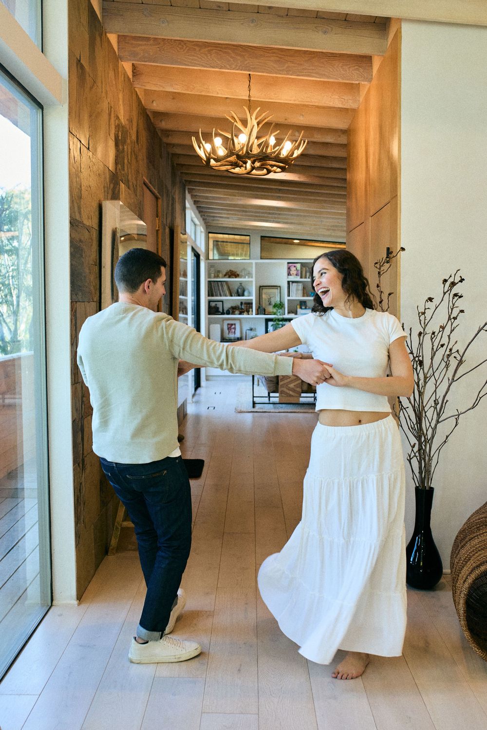A couple dancing joyfully in a modern rustic room with wooden beams and an antler chandelier.