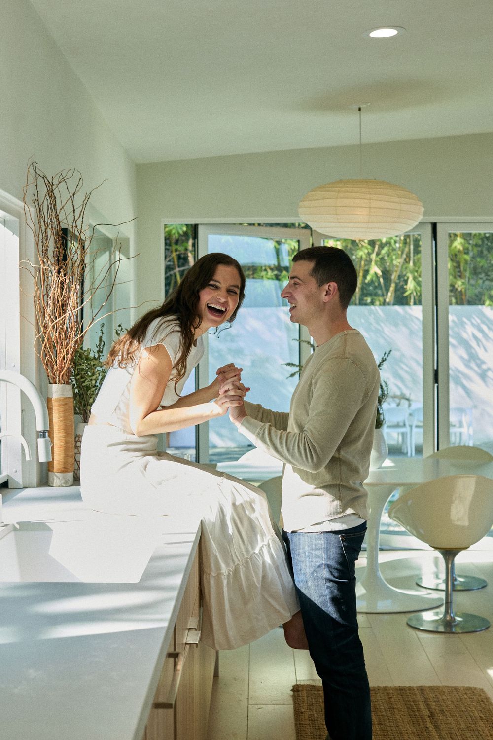A couple shares a joyful moment together in a bright modern kitchen with a paper lantern light fixture.