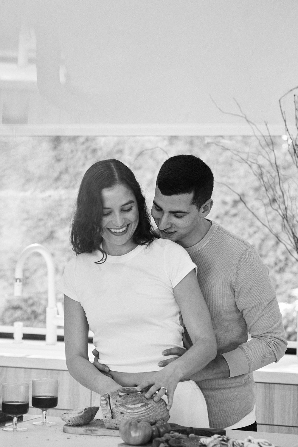 A romantic black and white photo showing a couple sharing an intimate moment while cooking together in a kitchen.