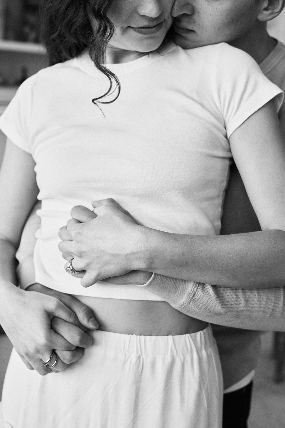 Intimate black and white photo showing a couple embracing, with hands clasped, wearing white casual clothing.