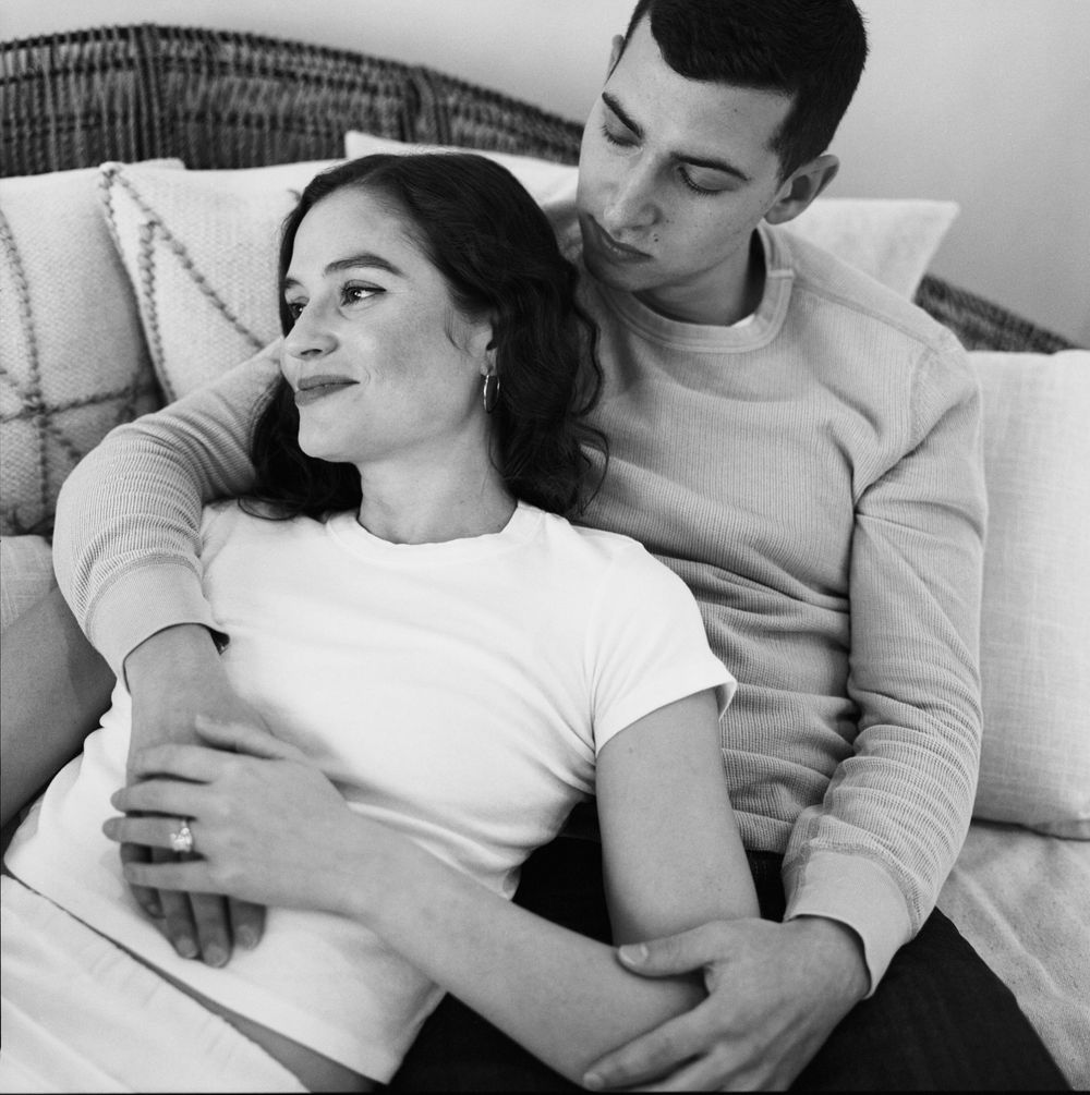 A romantic black and white photo of a couple cuddling together on a rattan couch.