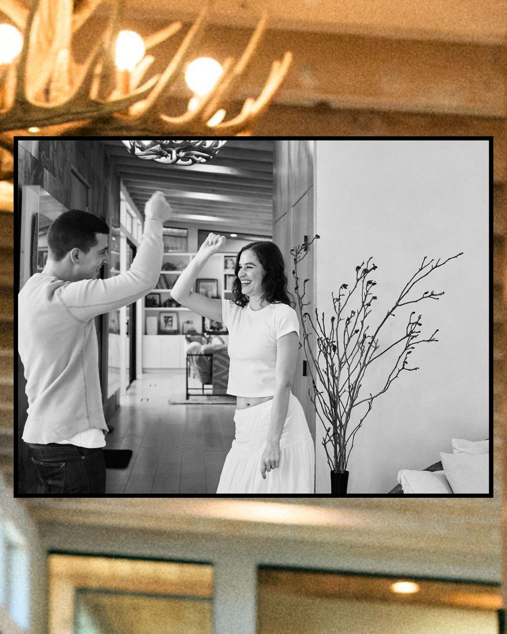 A black and white candid photo of two people giving each other a high five in an indoor setting with decor visible.