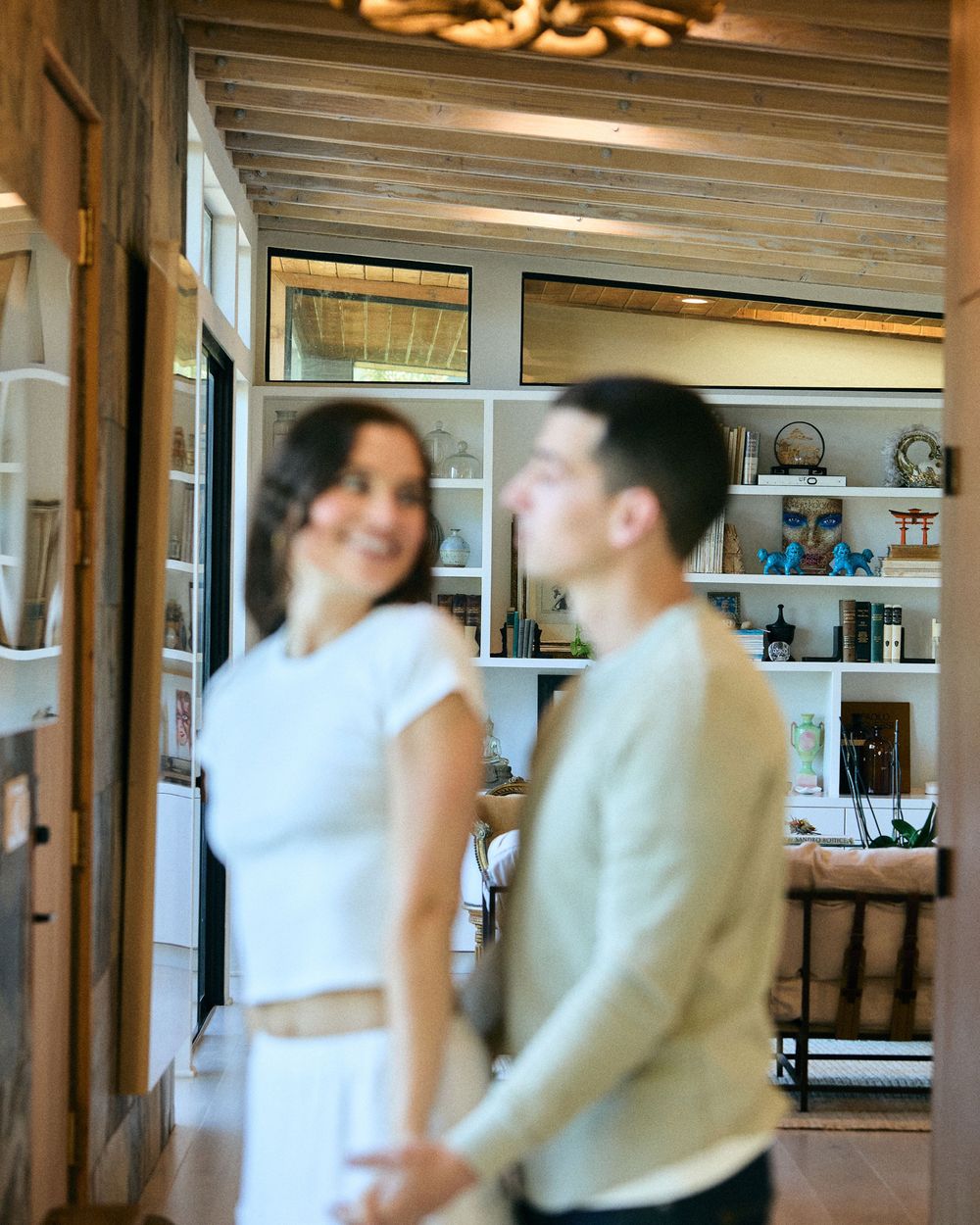 A candid moment between a couple laughing together in a rustic interior with wooden beams and shelving.