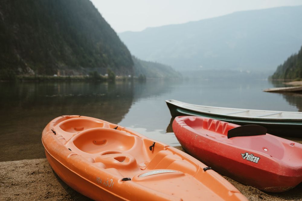 Orange and red kayaks rest on the shore of a tranquil mountain lake.