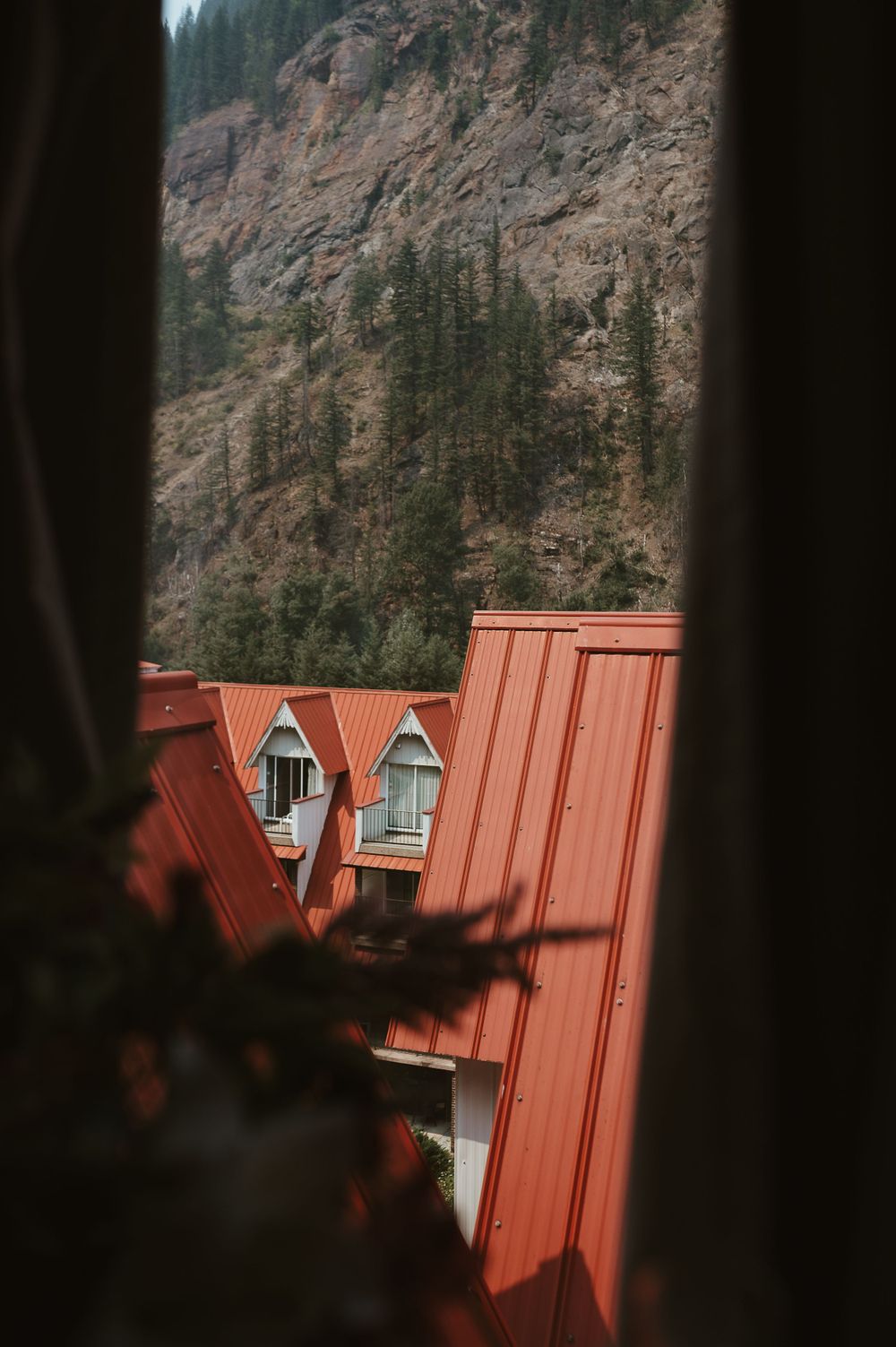 View of red-roofed mountain lodge nestled against rocky cliff and evergreen forest.