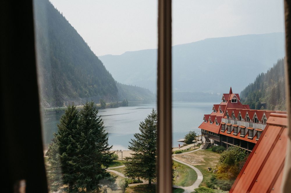 Scenic view of a rustic red lodge overlooking a serene mountain lake through a window frame.