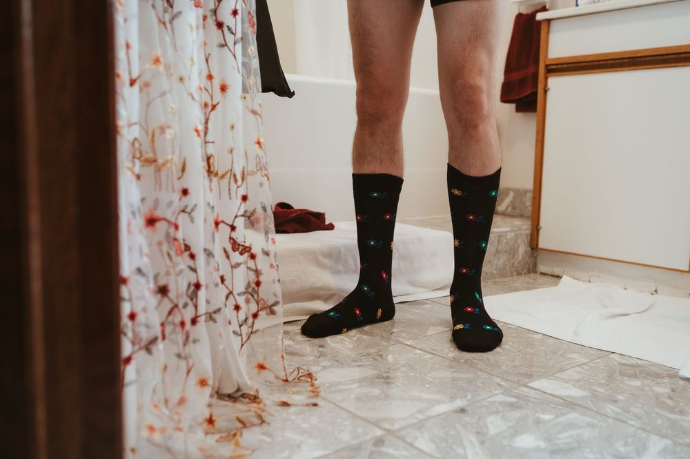 Black dress socks against floral curtain background on tile floor.