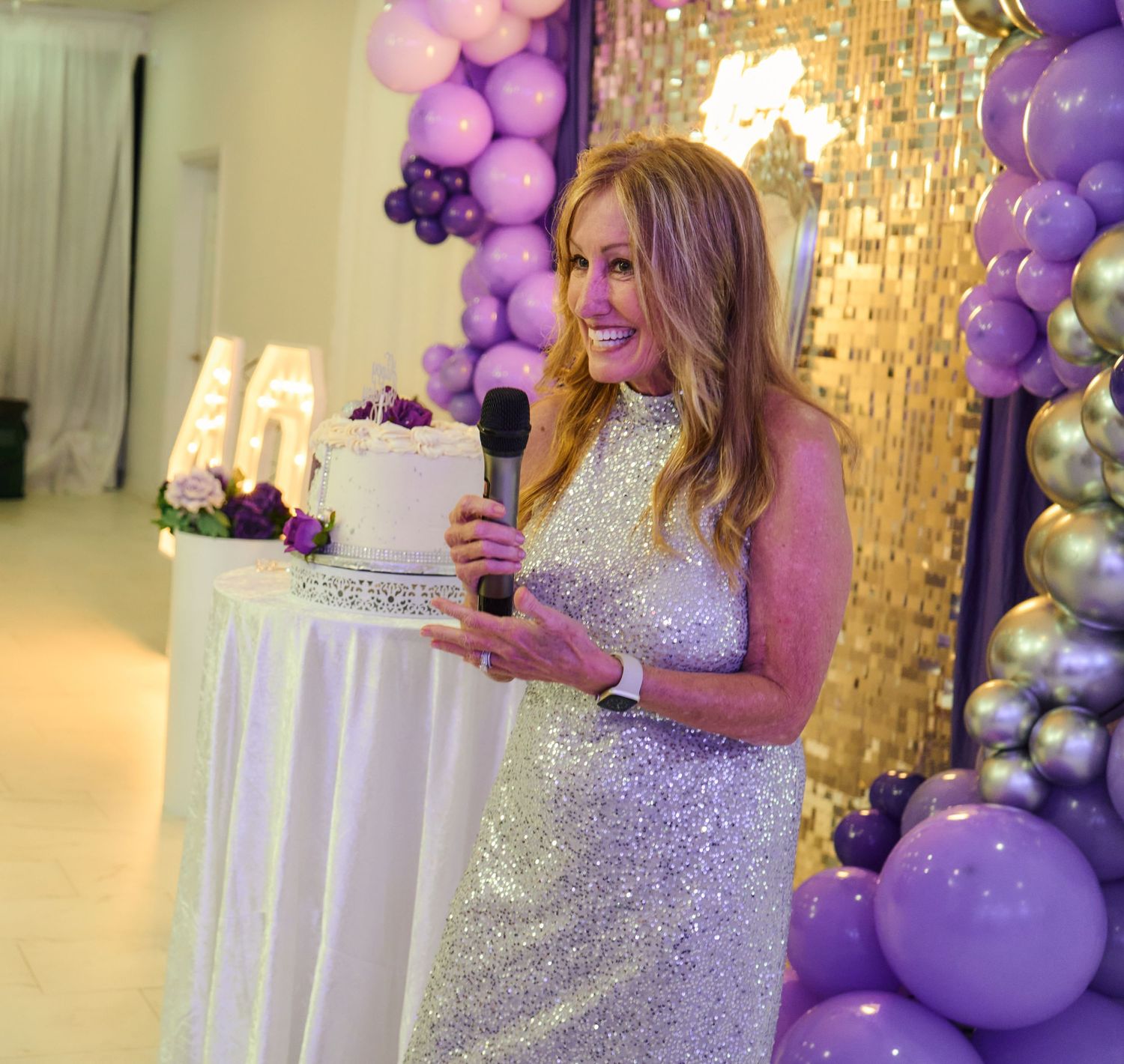 An elegant celebration setup with purple and silver balloons against a gold sequin backdrop.