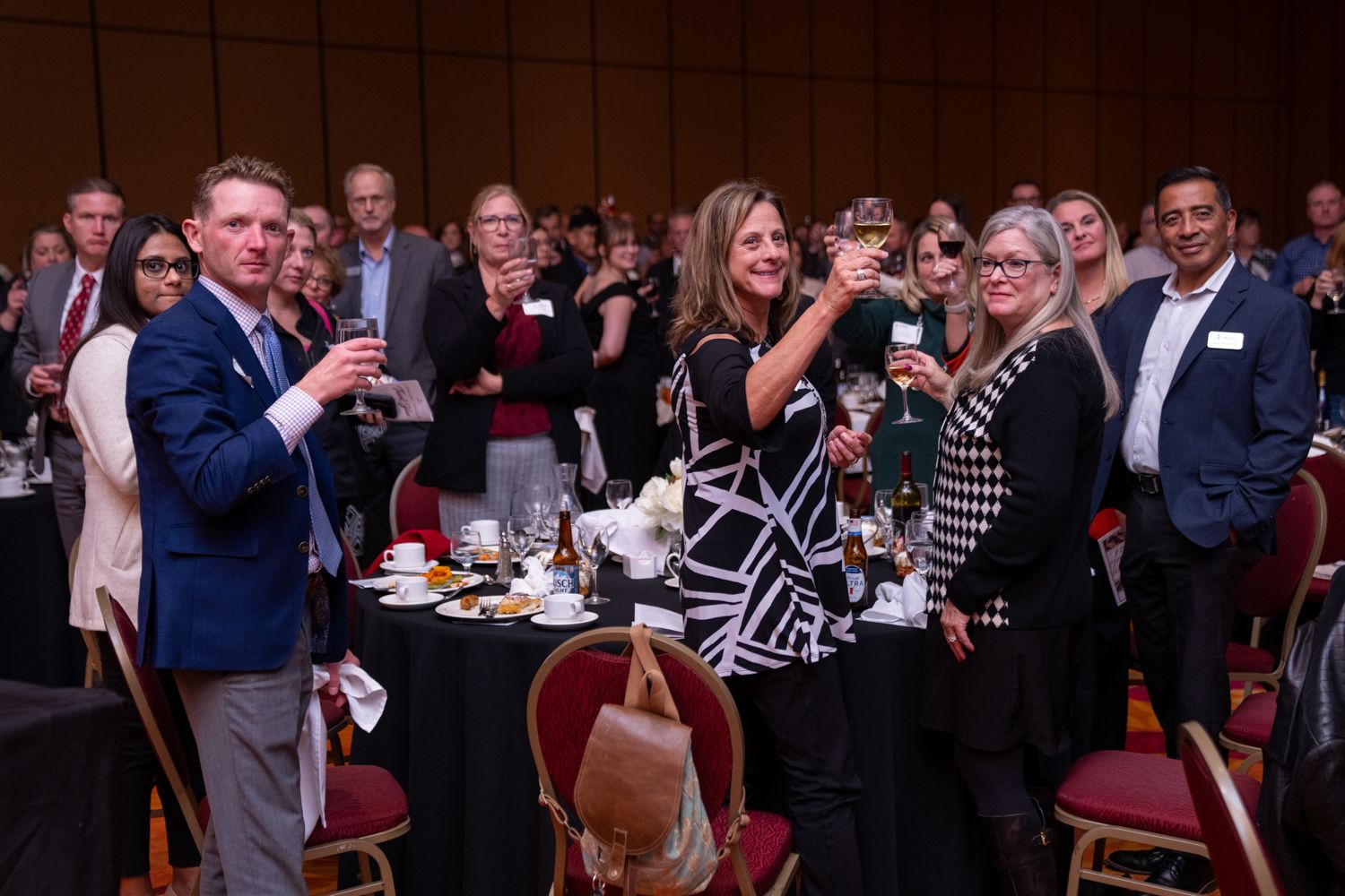 Crowd of people at a formal dinner event raising glasses in celebration.