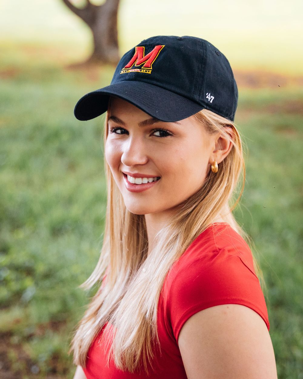 Outdoor portrait photography session featuring red athletic wear and a baseball cap.