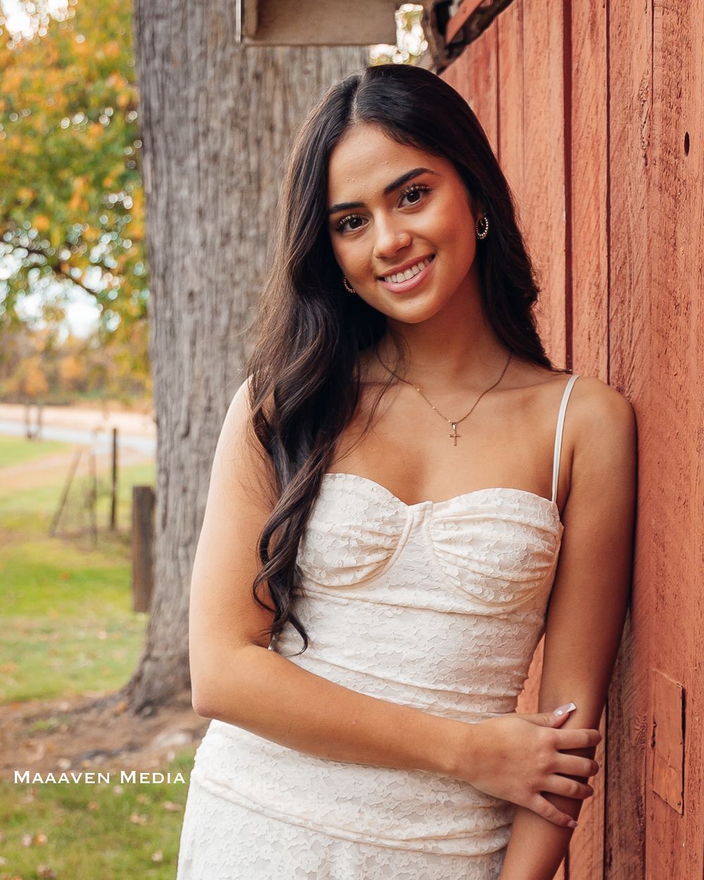 A person in a white dress poses against a rustic wooden wall during an autumn outdoor photo session.