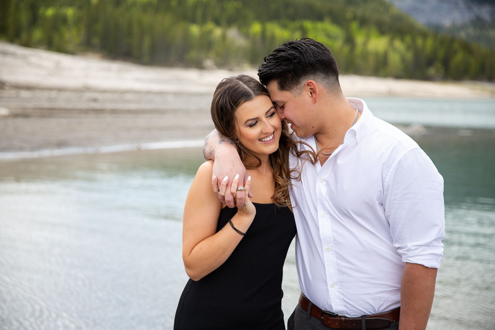Romantic couple embracing by mountain lake with forest backdrop.