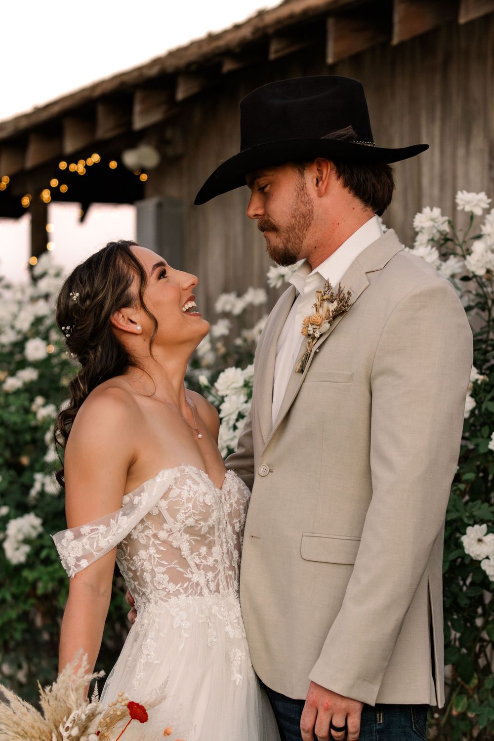 Romantic wedding portraits against a rustic wall with white flowers and string lights.