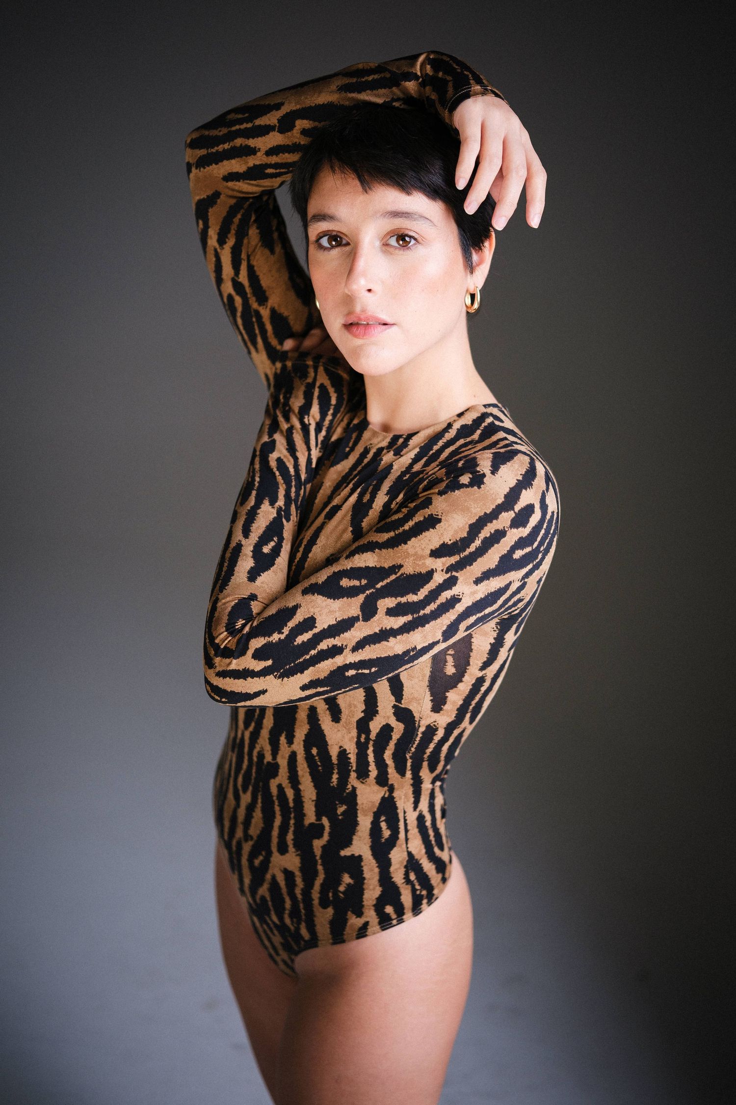 Model poses in tiger stripe pattern top against dark studio backdrop.