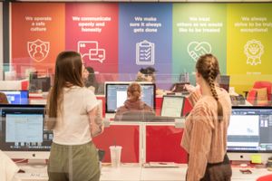 People interact at a colorful retail counter with digital displays and rainbow-colored wall graphics showing company values.