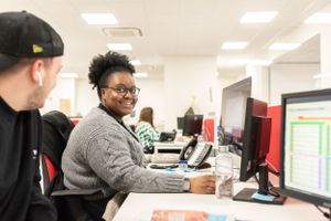 Students work together at computer workstations in a modern college computer lab setting.